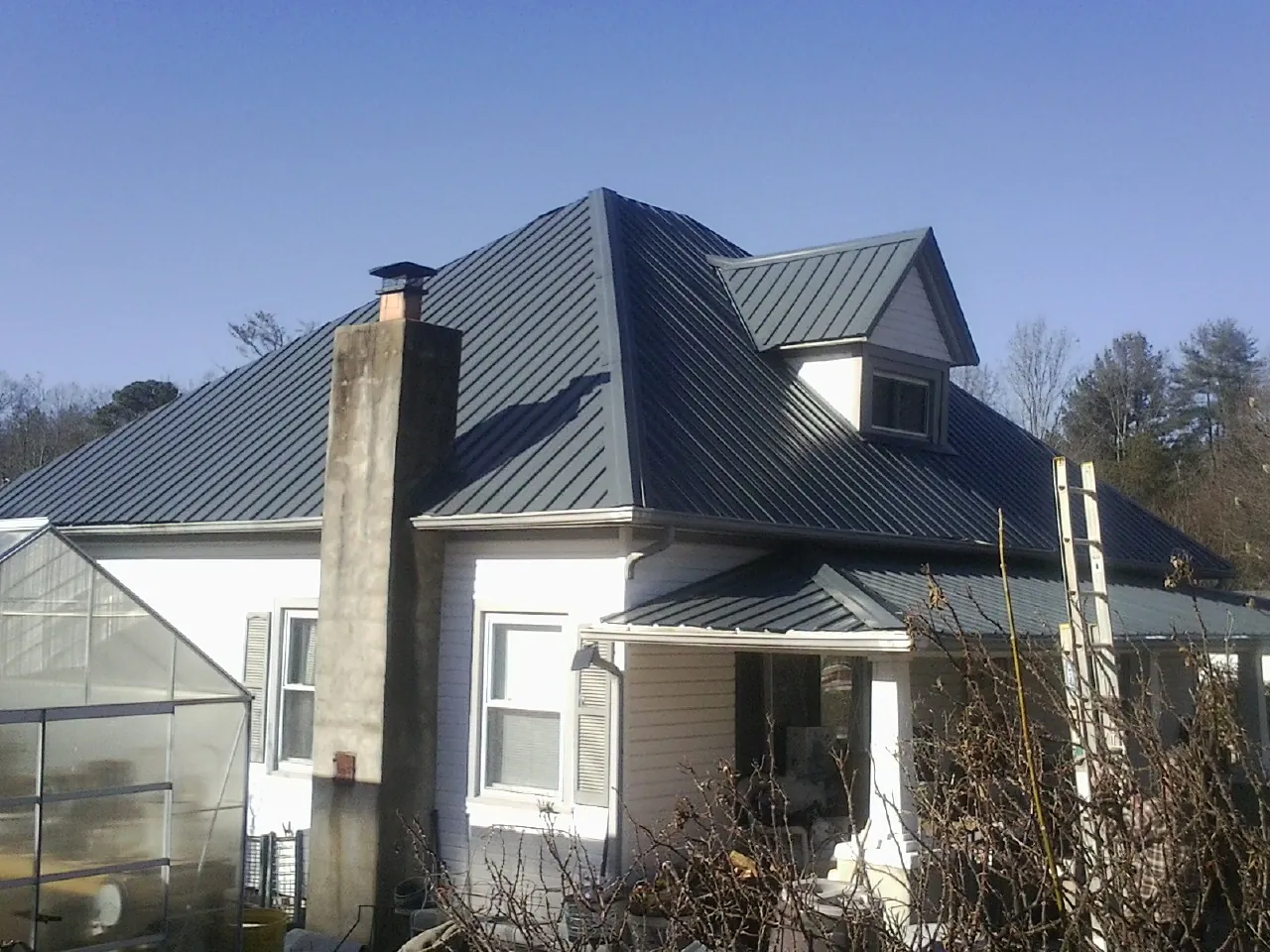 Dark blue standing seam metal roof on a white farmhouse with dormer in Benge