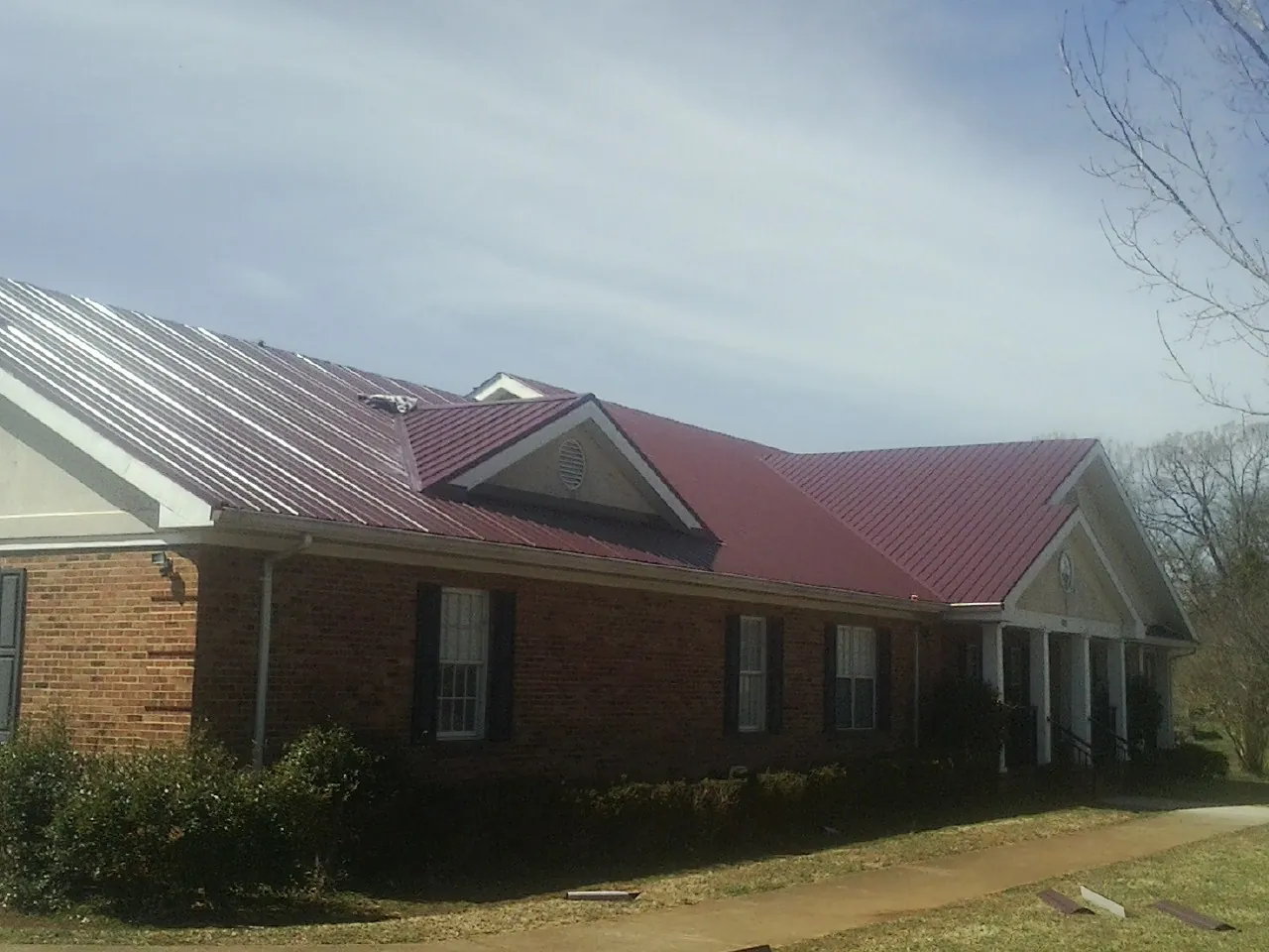 Red metal roof with gabled entries on a long brick building, from a Hail Damage Roof Repair job in Benge
