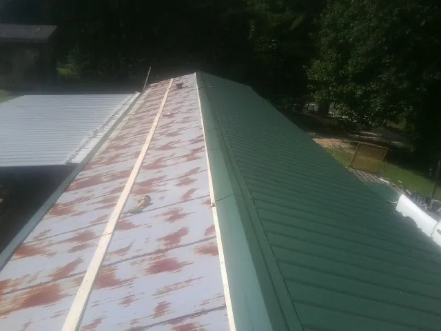Old rusted panels beside newly installed green metal roofing — Wind Damage Roof Repair by Roofing Brothers in Benge