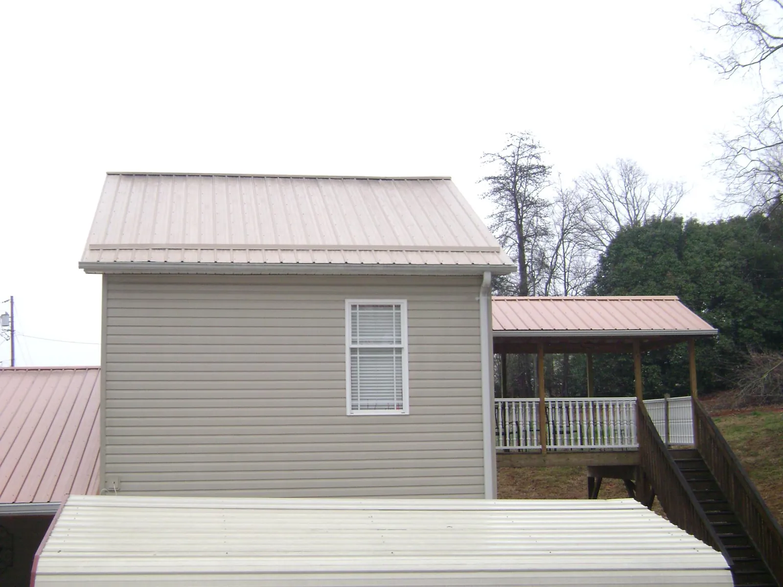 Tan metal roofs on a two story addition and attached porch, from a Roof Replacement job in Benge